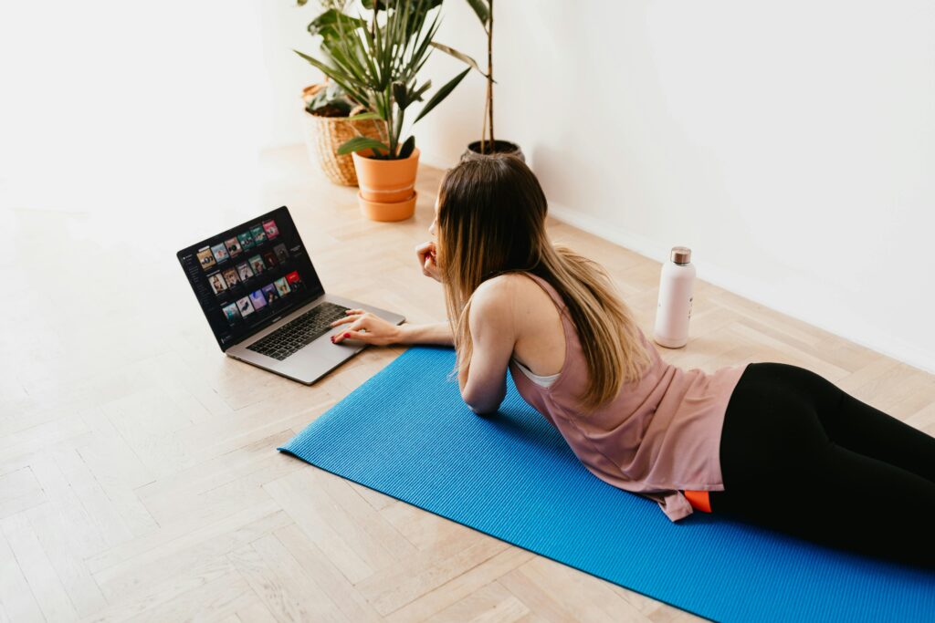 Young woman lying on floor on mat while using laptop at home